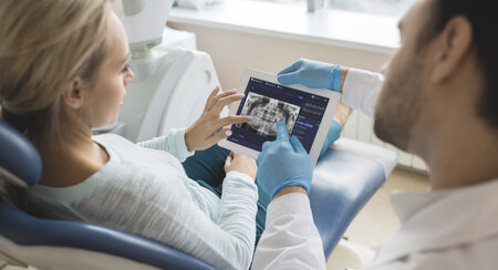 A man shows a woman an x-ray of her teeth on a tablet
