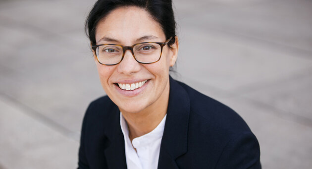 Woman with glasses in black blazer in front of grey background