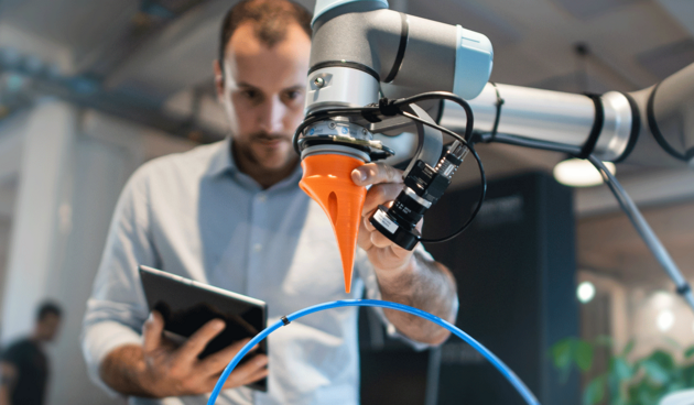 Mann mit Tablet in der Hand bedient einen Roboterarm im Vordergrund.
